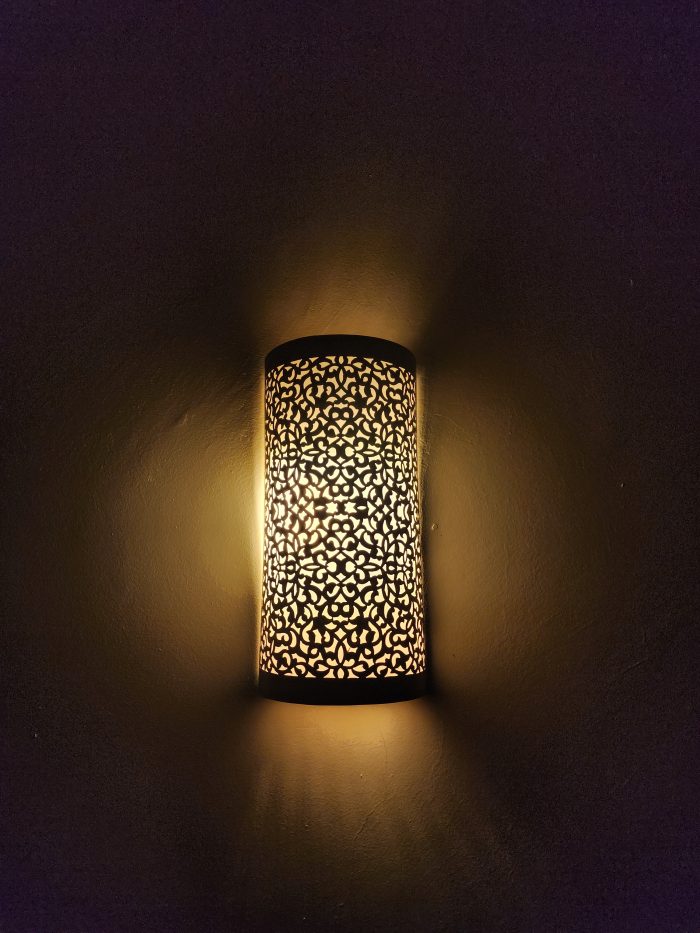 Handmade filigree brass wall sconce with intricate floral cutout pattern and warm ambient wall lighting.