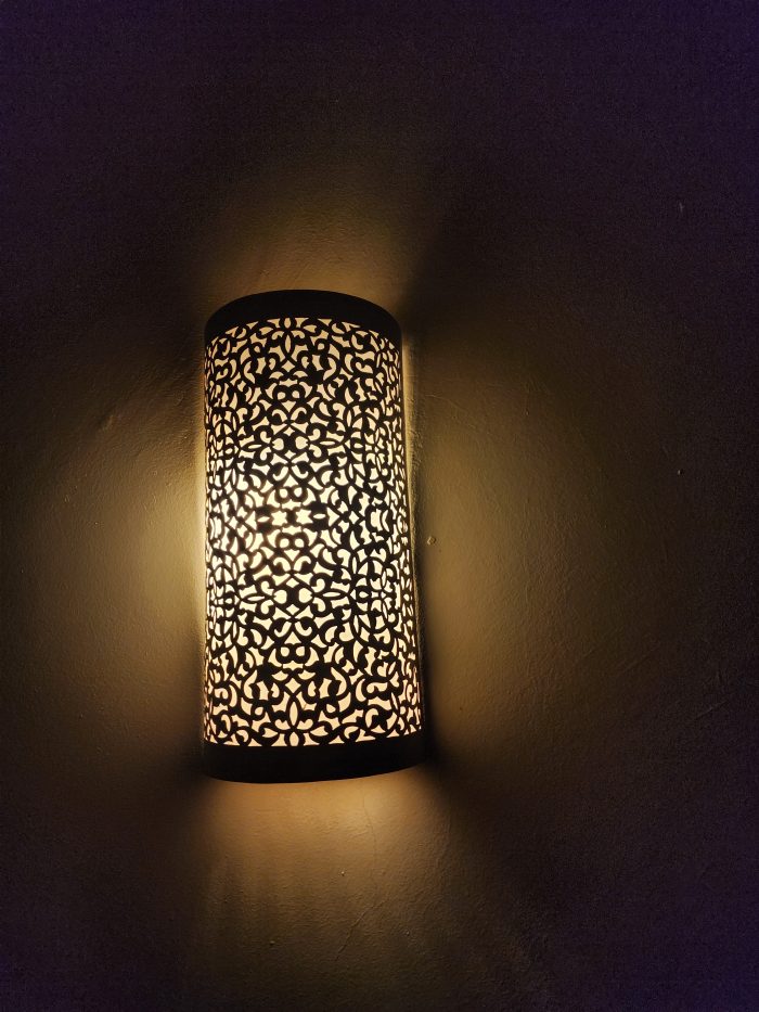Handmade filigree brass wall sconce with intricate floral cutout pattern and warm ambient wall lighting.