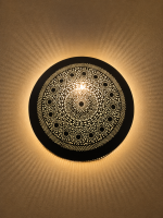Handmade round brass wall light with intricate mandala pattern and radiant warm halo illumination.