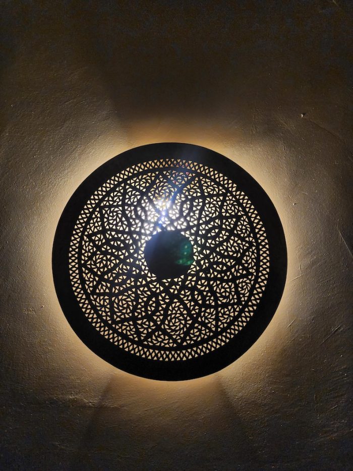 Handmade round brass wall light with floral rosette openwork, solid center medallion and warm glowing halo.