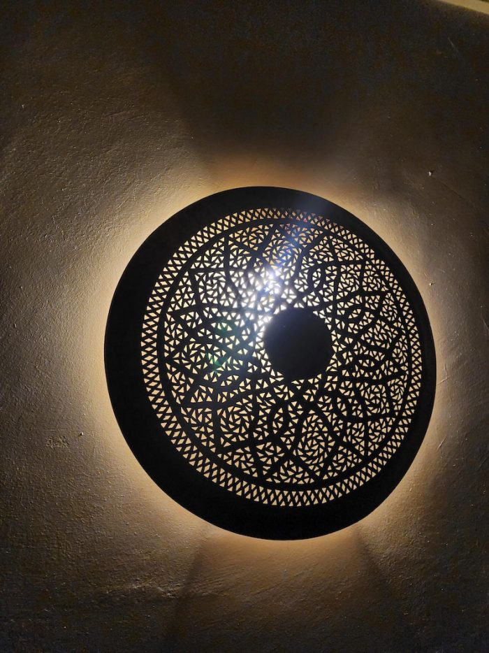 Handmade round brass wall light with floral rosette openwork, solid center medallion and warm glowing halo.