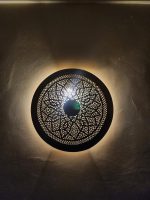 Handmade round brass wall light with floral rosette openwork, solid center medallion and warm glowing halo.