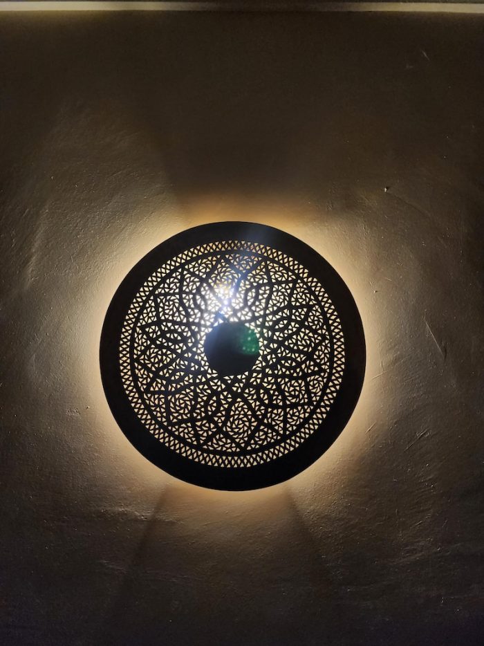 Handmade round brass wall light with floral rosette openwork, solid center medallion and warm glowing halo.
