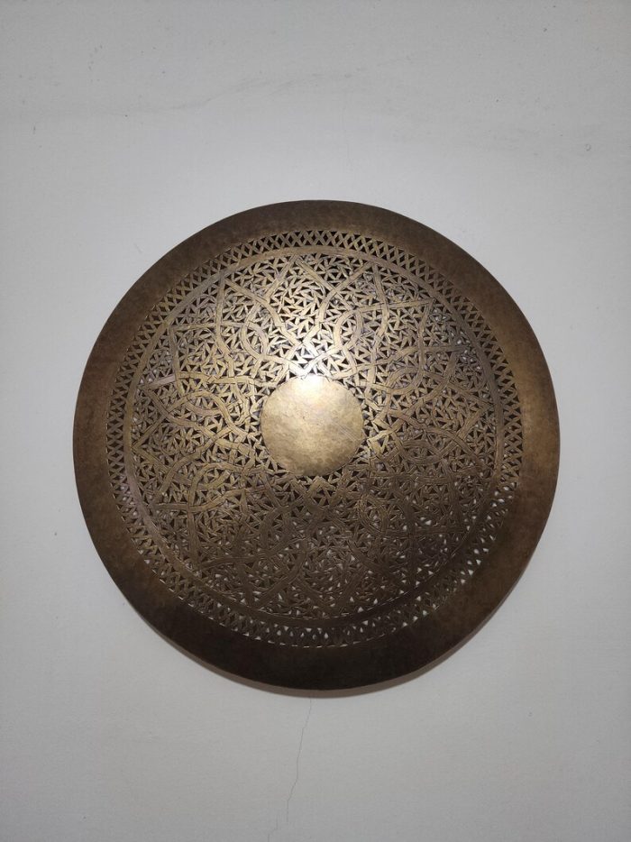 Handmade round brass wall light with floral rosette openwork, solid center medallion and warm glowing halo.