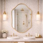 Handmade sculpted oval brass wall mirror with flowing curved edges and solid brass frame above double bathroom vanity.