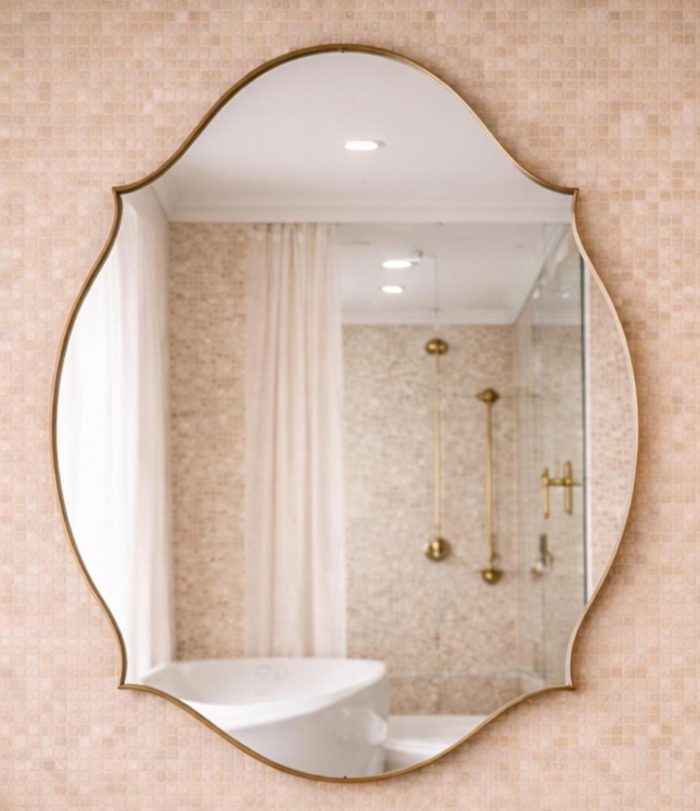 Handmade curved crown brass wall mirror with scalloped edges and solid brass frame above bathroom vanity.