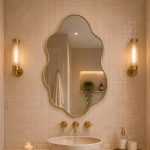 Handmade sculptural wavy brass wall mirror with clear glass and slim solid brass frame displayed above a modern bathroom vanity.