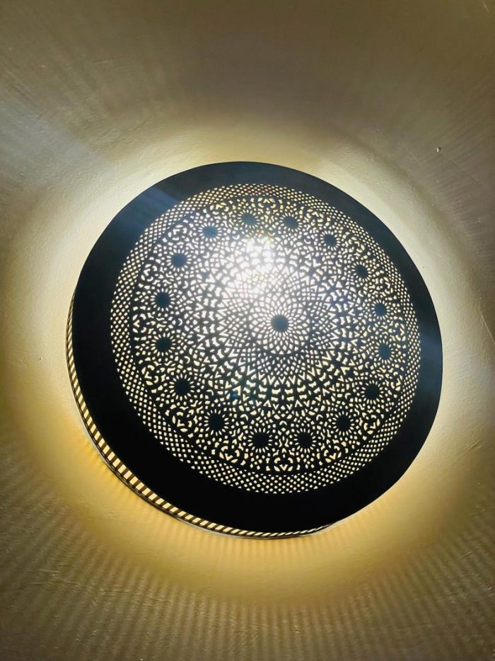 Handmade round brass wall light with intricate mandala pattern and radiant warm halo illumination.