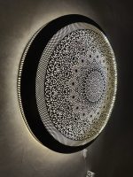 Handmade Moroccan brass wall light with round pierced floral design and warm halo illumination.