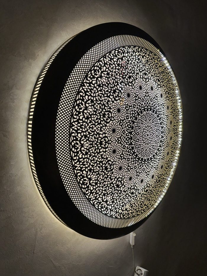 Handmade Moroccan brass wall light with round pierced floral design and warm halo illumination.