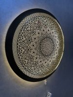 Handmade Moroccan brass wall light with round pierced floral design and warm halo illumination.