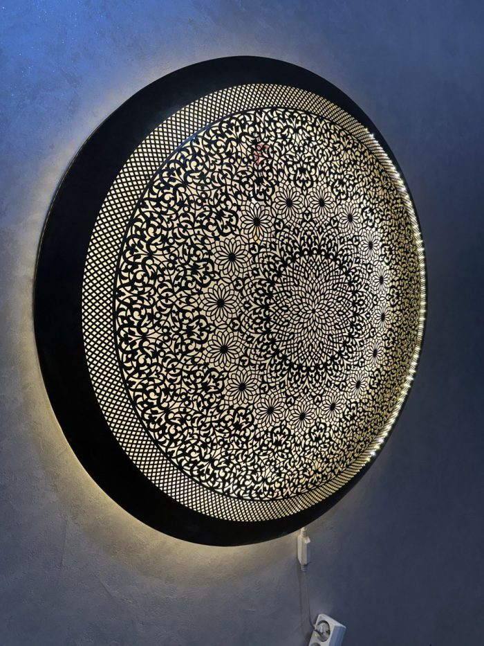 Handmade Moroccan brass wall light with round pierced floral design and warm halo illumination.